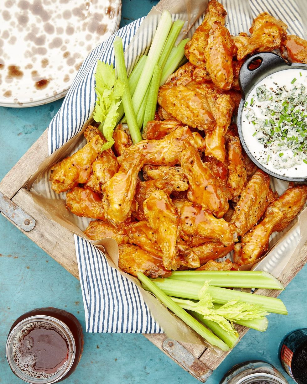 spicy oven baked buffalo wings on a wooden serving tray with a bowl of blue cheese dip and celery sticks