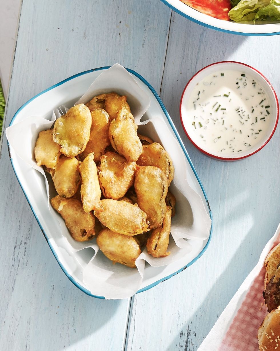 fried pickles in a serving dish lined with parchment paper with a little bowl of buttermilk ranch on the side for dipping