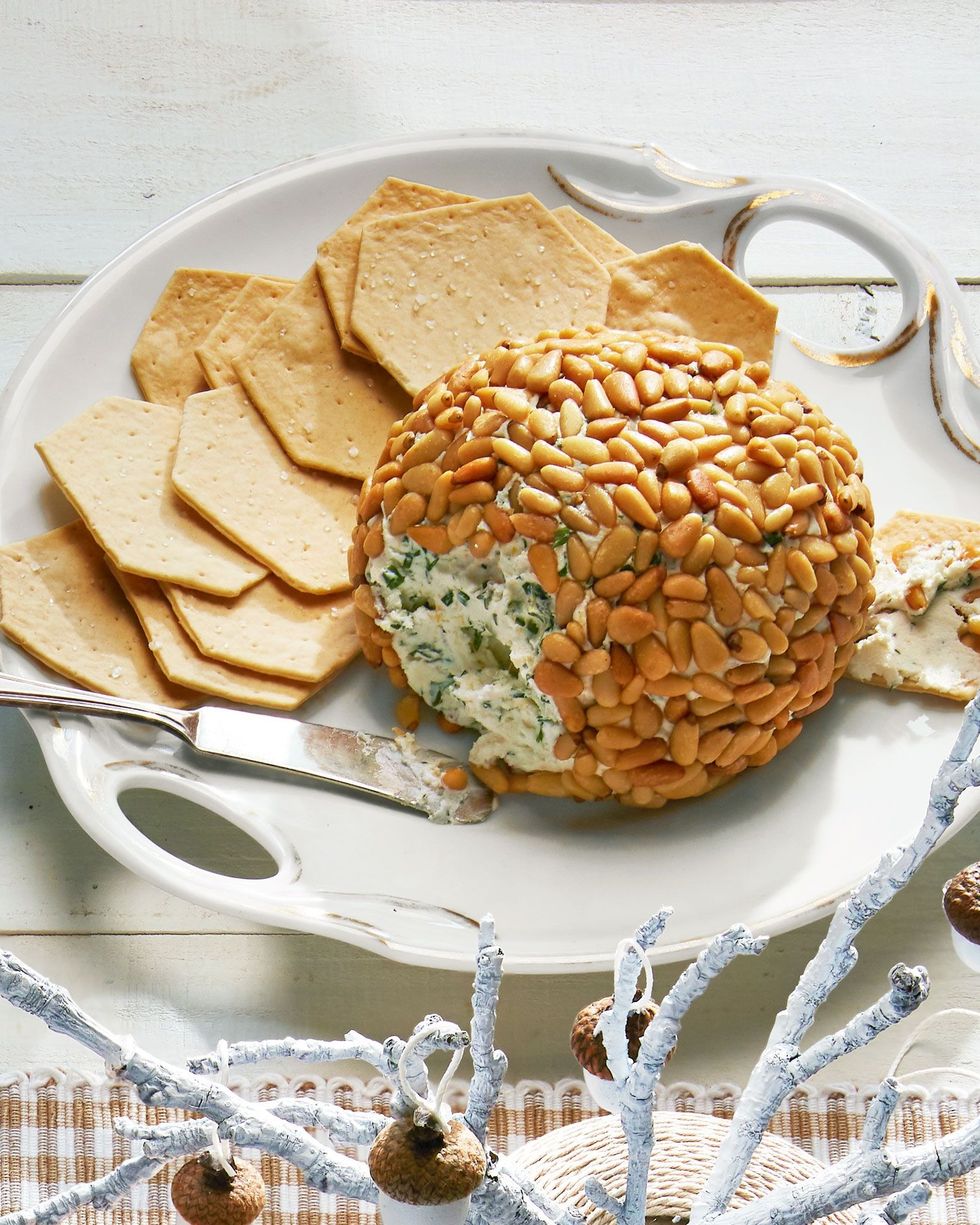 herbed cheese ball covered in toasted pine nuts on a white plate with crackers