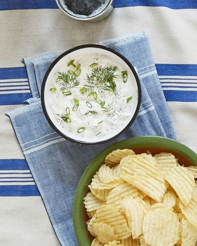 dill scallion dip in a bowl with sliced green onions and dill on top with a bowl of chips on the side